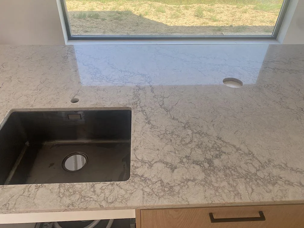 Köksbänkskiva i Caesarstone Moorland Fog, polerad kvartskomposit, med svart underlimmad diskho, kranhål och mjuk grå ådring i Farhult.