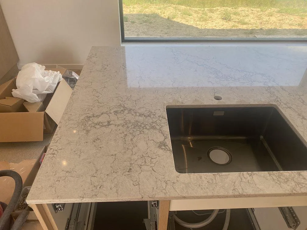 Polerad köksbänkskiva i Caesarstone Moorland Fog med svart underlimmad diskho och ljusgrå ådring under montering i Farhult.