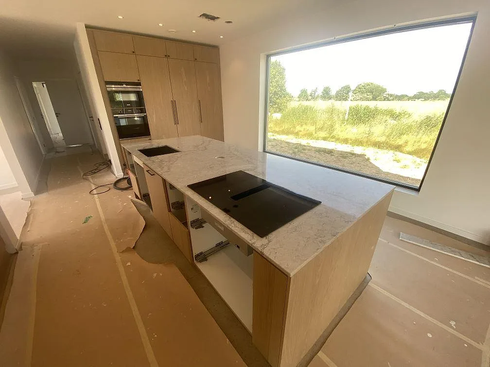 Köksö och bänkskiva i Caesarstone Moorland Fog, polerad ljusgrå kvartskomposit, med svart induktionshäll och stor fönstervy i ett kök i Farhult.