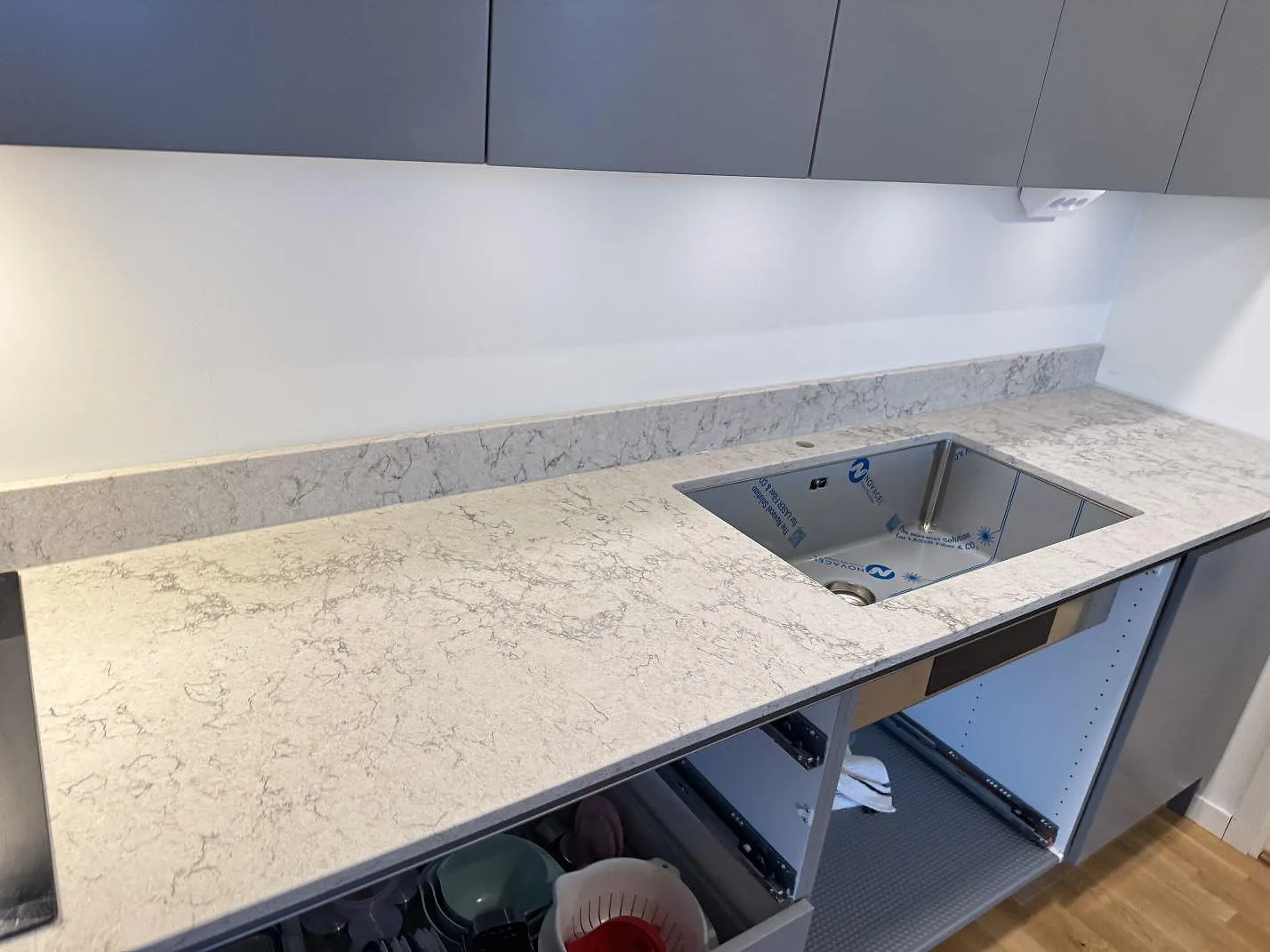 Polerad köksbänkskiva i Caesarstone Moorland Fog med underlimmad rostfri diskho och uppvikt stänkkant i samma sten, fotograferad i ögonhöjd i ett kök i Göteborg.