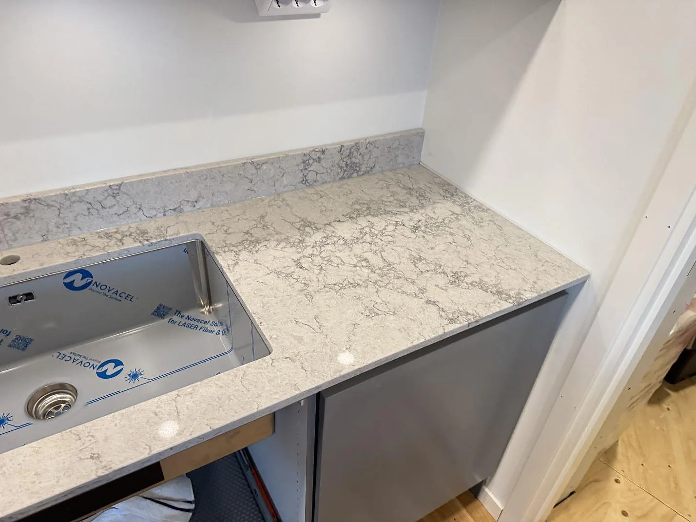 Underlimmad rostfri diskho i en polerad köksbänkskiva i Caesarstone Moorland Fog med uppvikt stänkkant i ett kök i Göteborg.