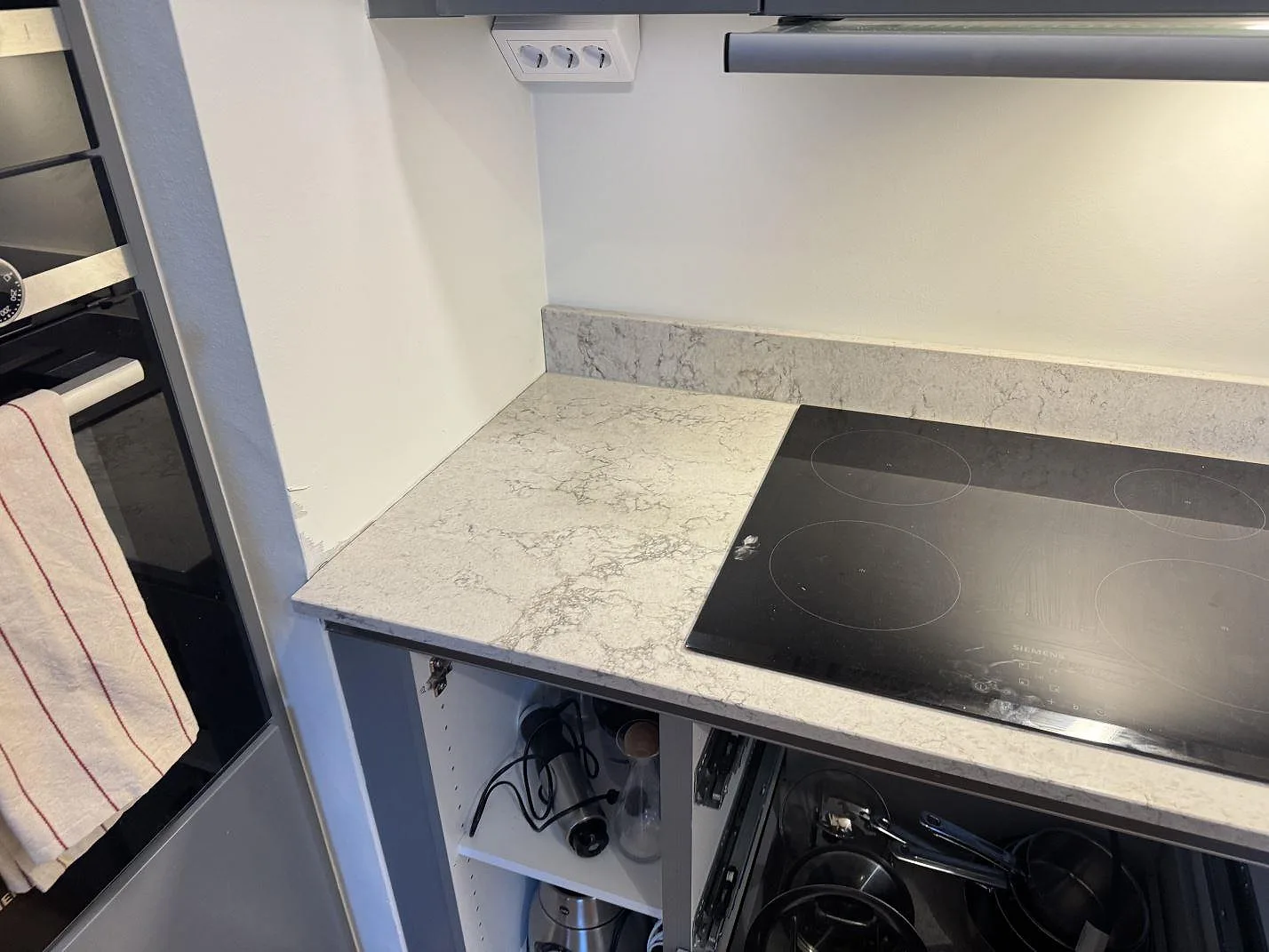 Köksbänkskiva i grå Caesarstone Moorland Fog med infälld Siemens induktionshäll och uppvikt stänkkant i ett kök i Göteborg.