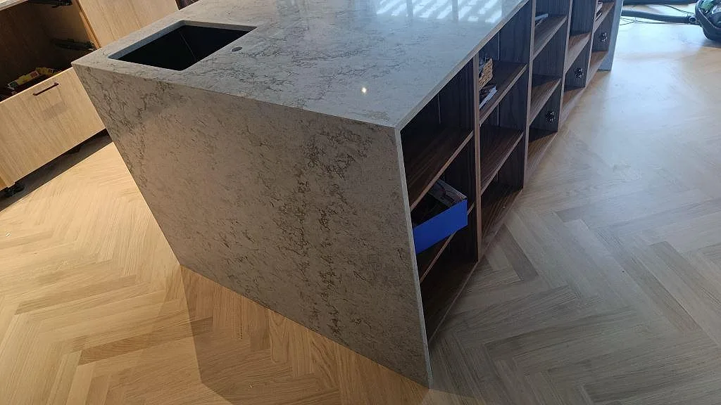Polerad köksö i Caesarstone Moorland Fog med vattenfallssida, svart diskho och trästommar i Höllviken.