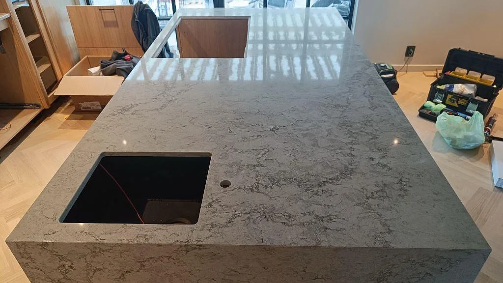 Köksö i polerad Caesarstone Moorland Fog med svart underlimmad diskho och urtag för häll i Höllviken.
