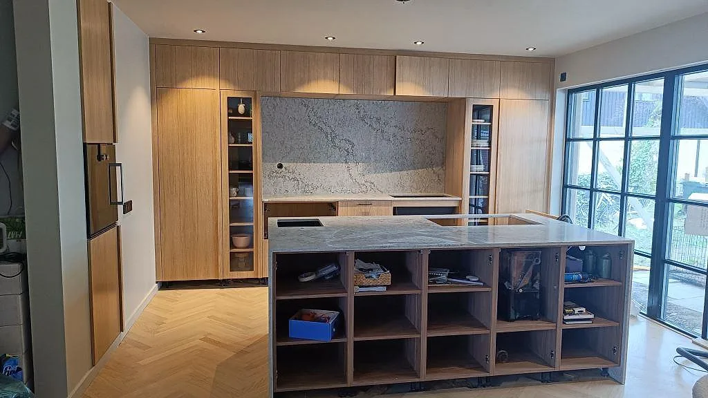 Köksbänkskiva i polerad Caesarstone Moorland Fog med köksö, stänkskydd och ljus träinredning i Höllviken.