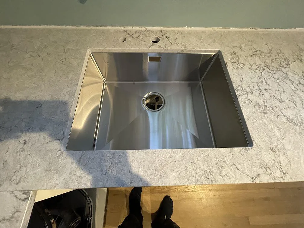 Underlimmad rostfri diskho infälld i polerad Caesarstone Moorland Fog bänkskiva, sedd ovanifrån, i ett kök i Huddinge.