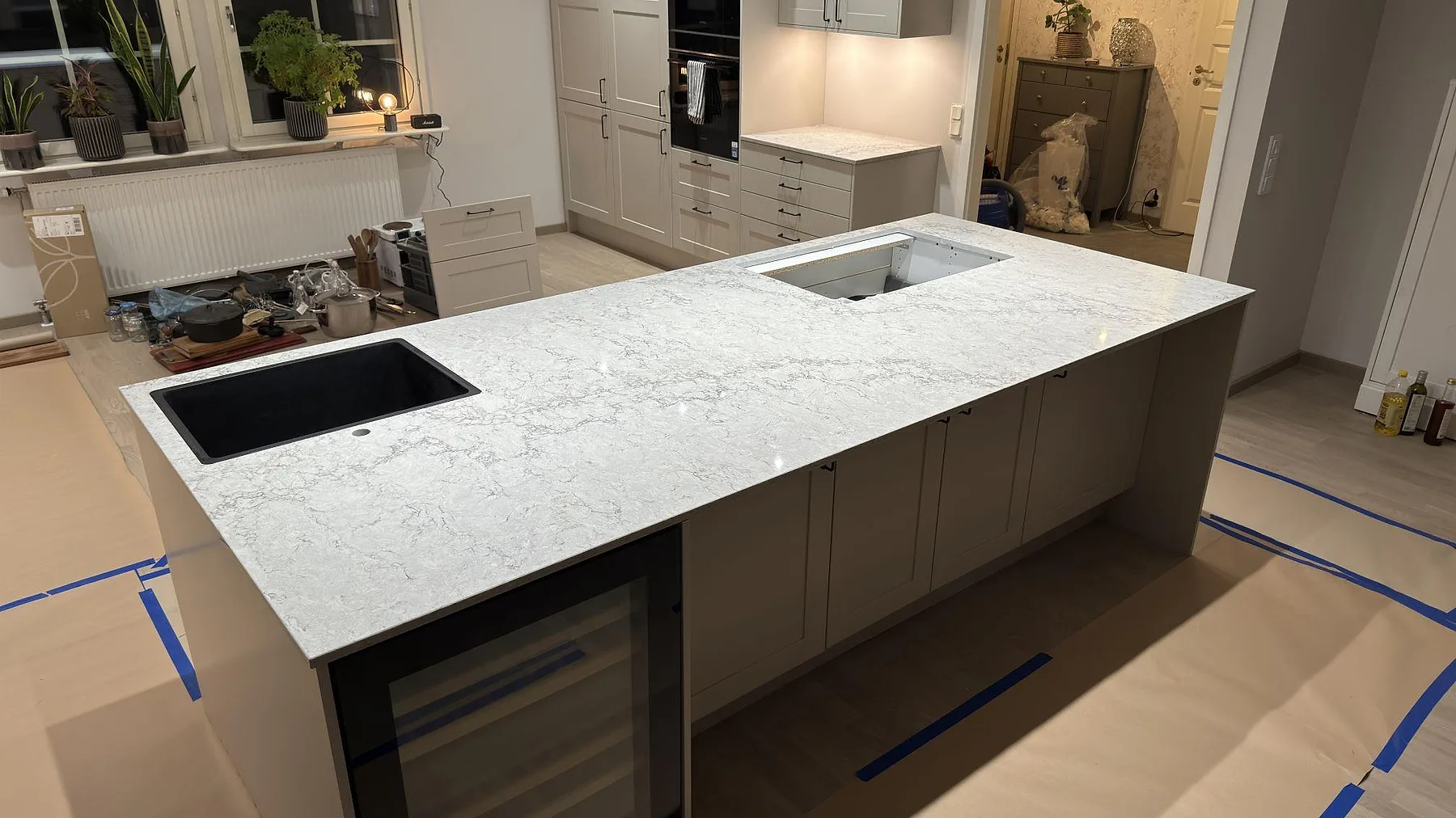 Ljusgrå köksö i Caesarstone Moorland Fog kvartskomposit med svart diskho och hällurtag under montering i ett kök i Knivsta.