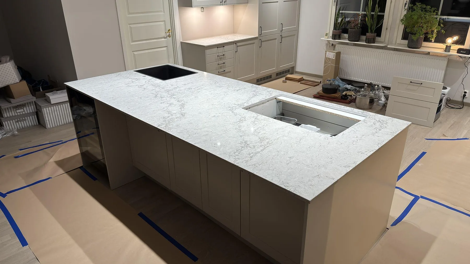 Köksö i Caesarstone Moorland Fog med polerad grå yta, underlimmad svart diskho och plats för infälld häll, sett från sidan i ett kök i Knivsta.