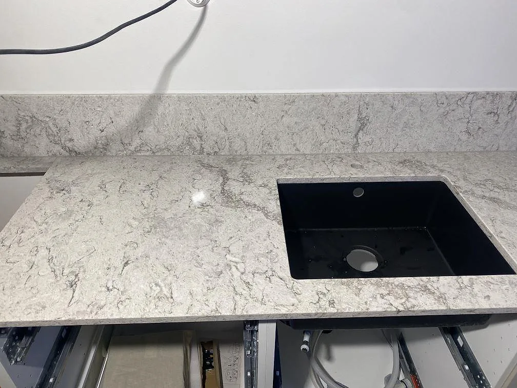 Svart underlimmad komposithoar i en polerad köksbänkskiva av Caesarstone Moorland Fog, i ett kök i Limhamn.
