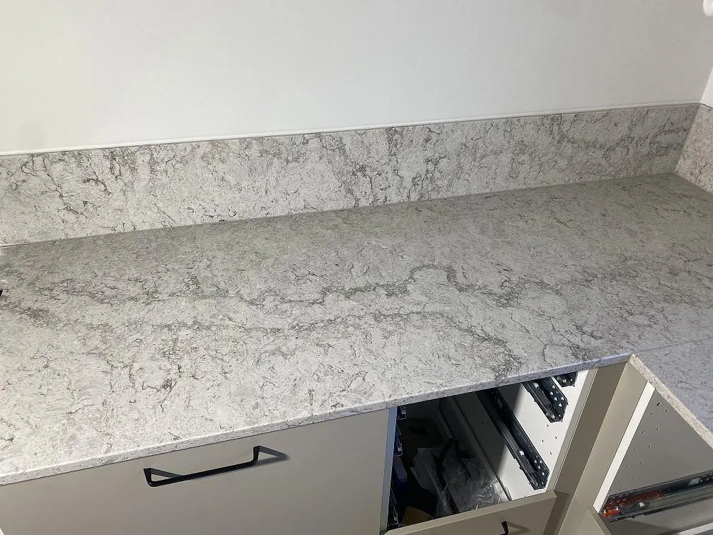 Lång köksbänkskiva i ljus Caesarstone Moorland Fog med tydlig grå ådring och uppvikt stänkkant ovanför stommarna, i ett kök i Limhamn.