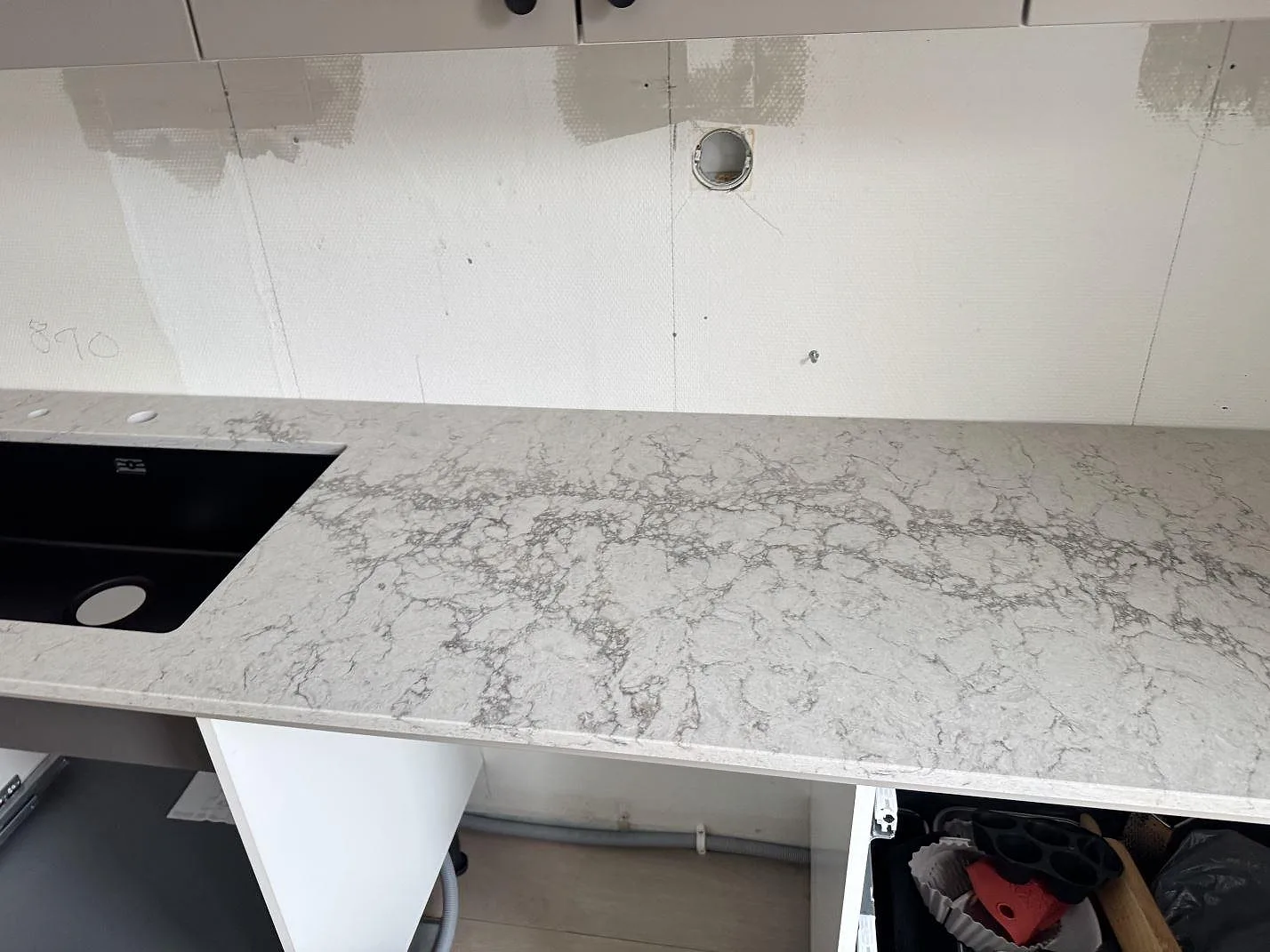 Väggbänk i Caesarstone Moorland Fog, polerad ljusgrå kvartskomposit, med svart diskho och öppna köksstommar under montering i Lund.