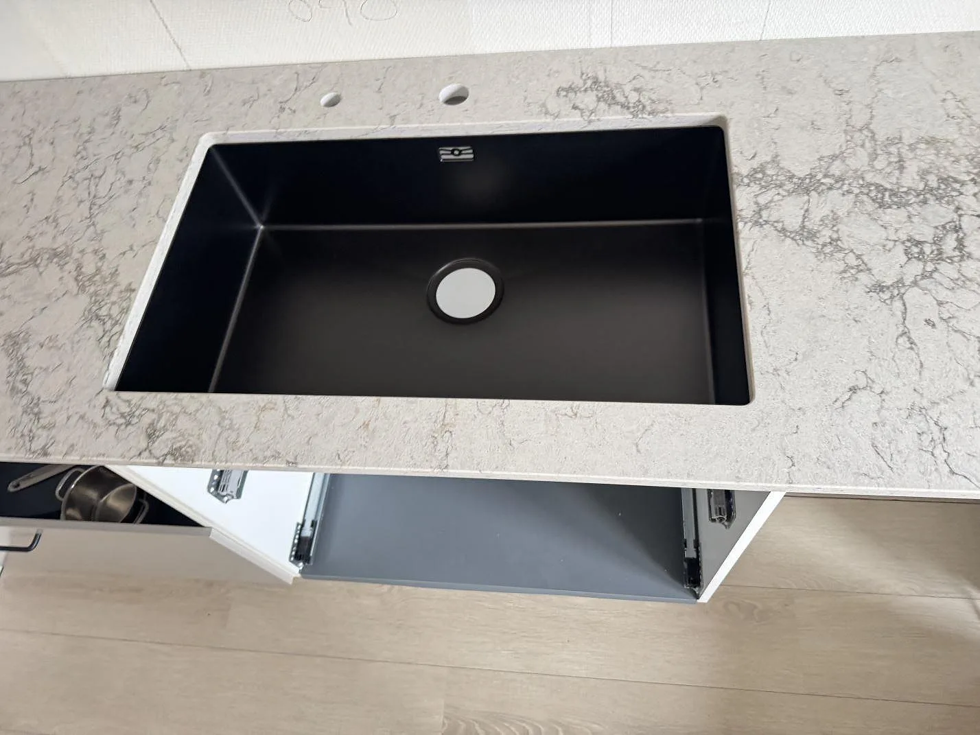 Svart diskho i en köksbänkskiva av Caesarstone Moorland Fog, polerad ljusgrå kvartskomposit med tydlig grå ådring i Lund.