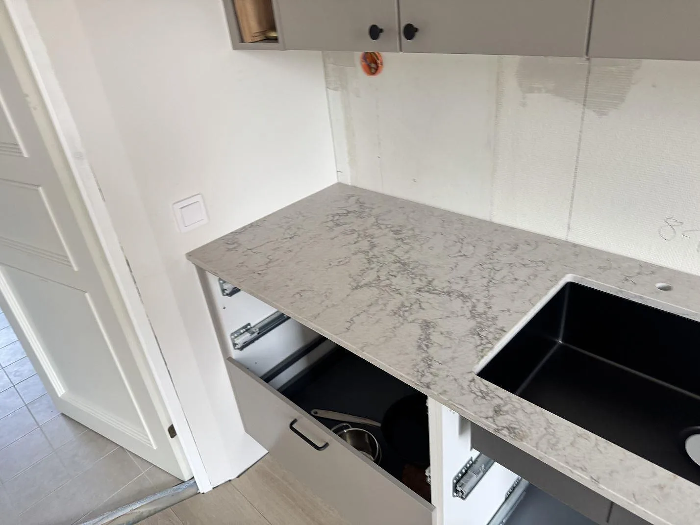 Sidovy av köksbänkskiva i Caesarstone Moorland Fog med svart diskho, polerad komposit och vägg som ännu inte är färdigställd i Lund.