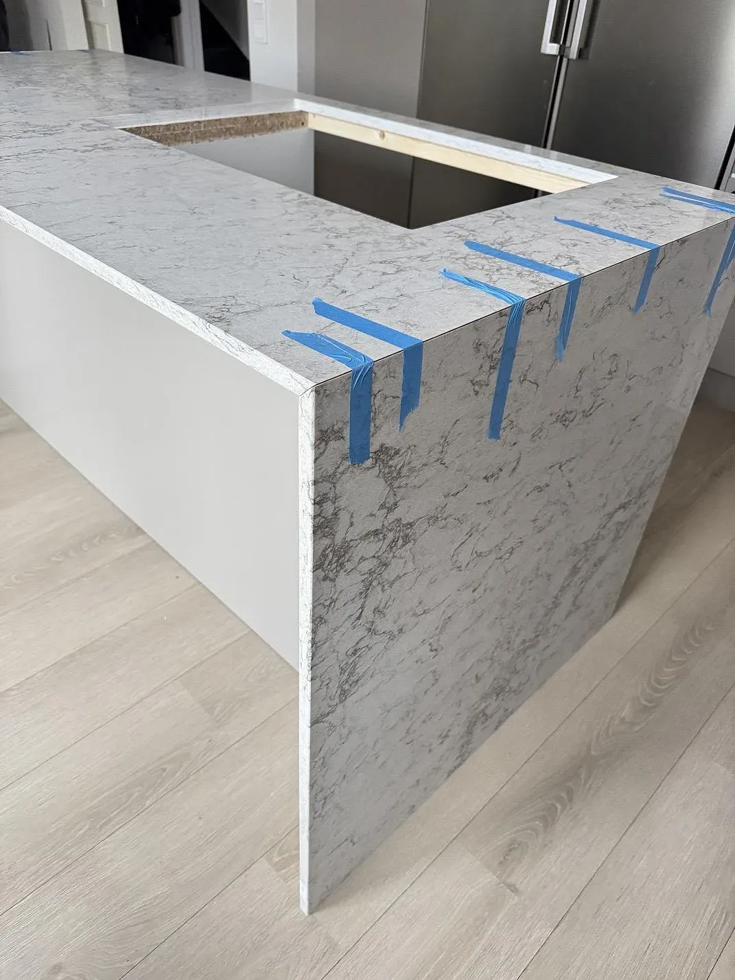 Närbild av köksö i Caesarstone Moorland Fog, polerad kvartskomposit, med nedvikt sida och blå monteringstejp i Lund.
