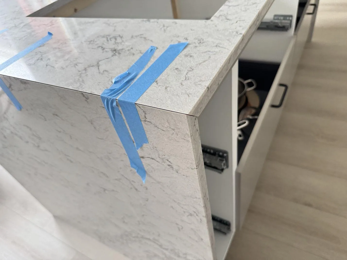 Närbild av kant och nedvikt sida i Caesarstone Moorland Fog, polerad ljusgrå kvartskomposit, med blå skyddstejp under montering i Lund.