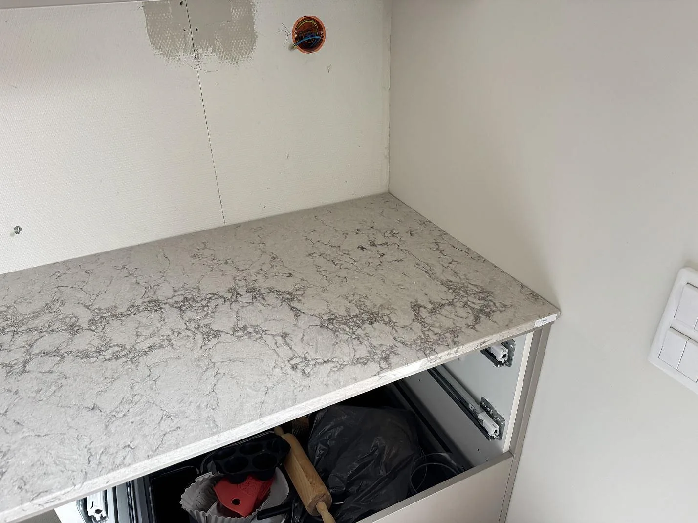 Hörndetalj av köksbänkskiva i Caesarstone Moorland Fog, polerad kvartskomposit med grå ådring, monterad över öppna stommar i Lund.