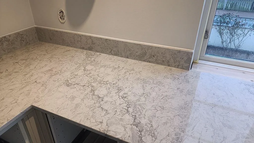 Polerad Caesarstone Moorland Fog bänkskiva med låg stänkkant och ljus fönsternisch i kök i Malmö.
