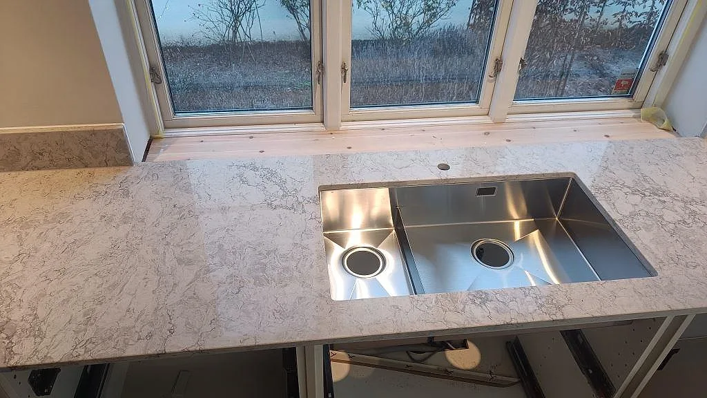 Underlimmad dubbelho i rostfritt stål i en polerad Caesarstone Moorland Fog bänkskiva vid fönster i Malmö.