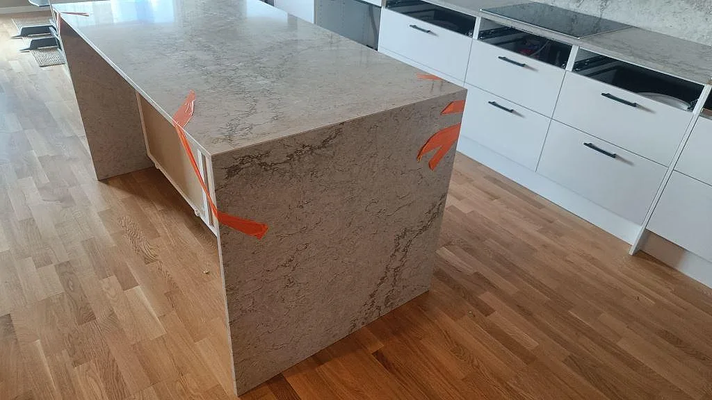 Köksö i polerad Caesarstone Moorland Fog med stenklädd gavel och ljus ådring under montering i Malmö.