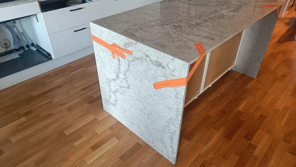 Närbild på köksö i polerad Caesarstone Moorland Fog med stenklädd sida och marmorerad ådring i Malmö.