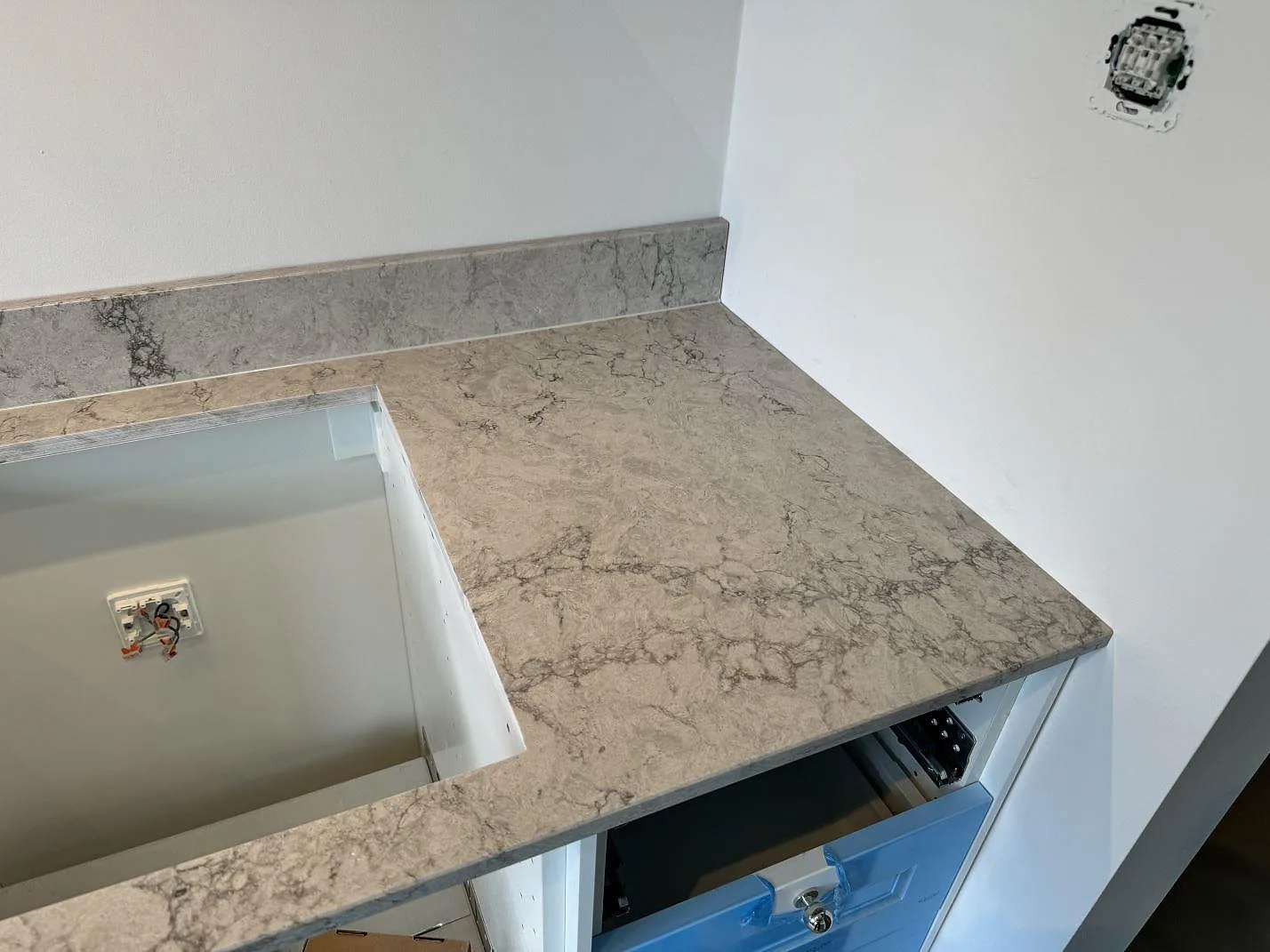Bänkskiva i Caesarstone Moorland Fog med polerad ljusgrå yta och uppvikt stänkkant bredvid ett förberett hällurtag i Malmö.
