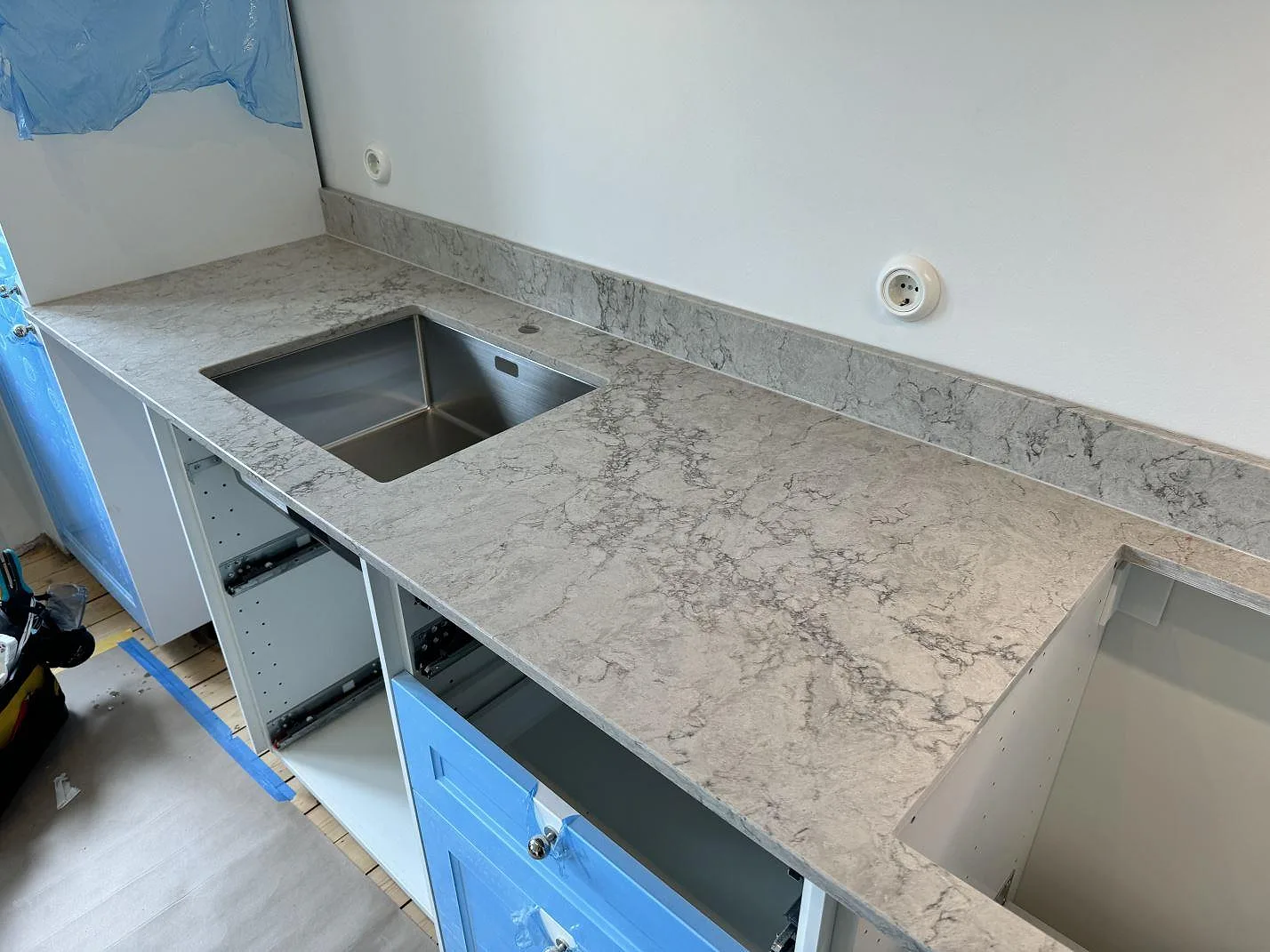 Lång köksbänk i Caesarstone Moorland Fog, polerad grå komposit, med rostfri diskho och förberett hällurtag under montering i Malmö.
