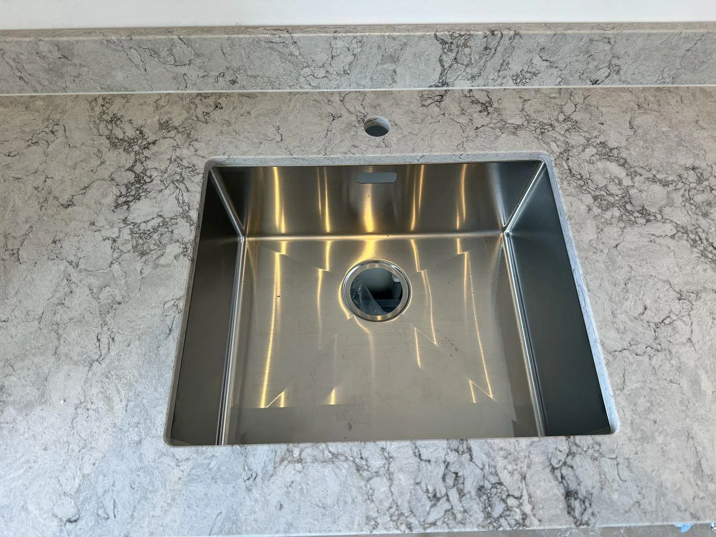 Rostfri diskho i en köksbänkskiva av Caesarstone Moorland Fog, polerad ljusgrå kvartskomposit med tydlig ådring i Malmö.