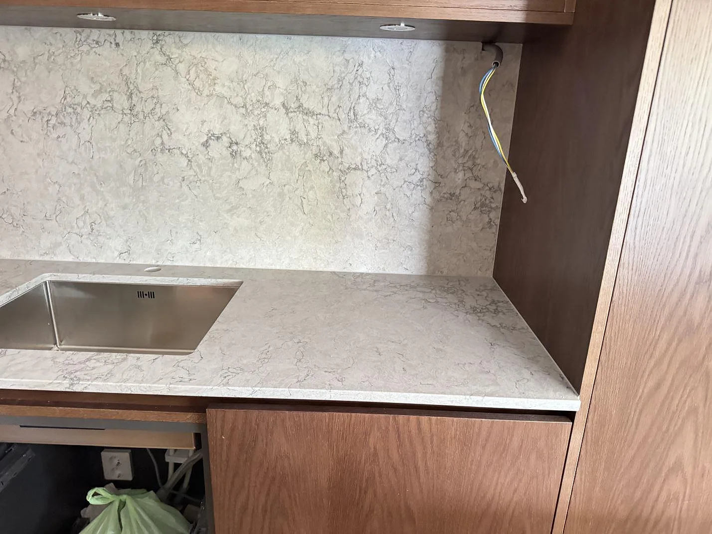 Närbild av polerad Caesarstone Moorland Fog som köksbänk med rostfri diskho, hög stenskiva bakom bänken och träinredning i Malmö.