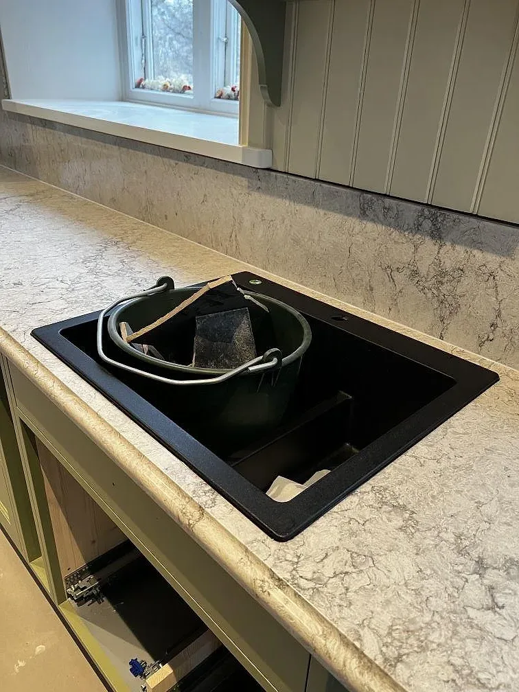 Svart underlimmad komposithoar i köksbänkskiva av polerad Caesarstone Moorland Fog i ett kök i Moheda.