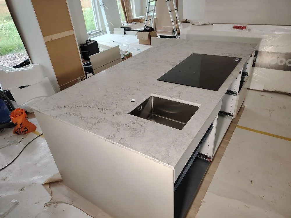 Köksö i Caesarstone Moorland Fog, polerad komposit med grå ådring, med svart häll och underlimmad rostfri diskho i ett kök i Örebro.