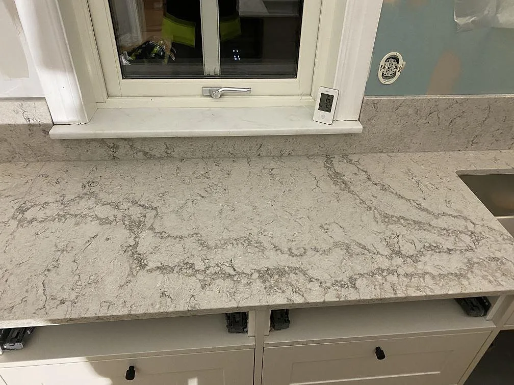 Bänkrad vid fönster med Caesarstone Moorland Fog, polerad kvartskomposit, uppvikt stänkkant och vit köksinredning i Sandared.
