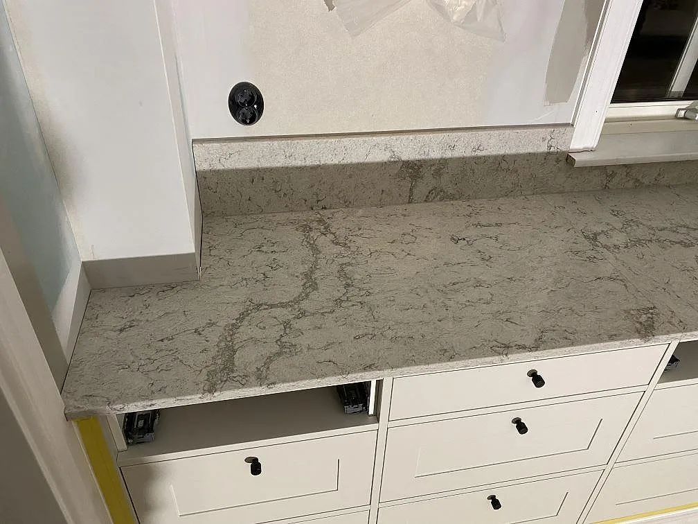Väggbänk i Caesarstone Moorland Fog med uppvikt stänkkant, polerad kvartskomposit och vita köksstommar i Sandared.