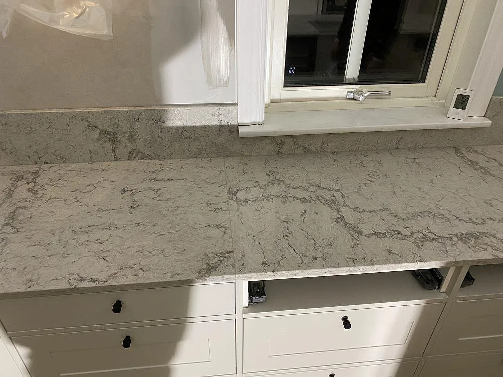 Polerad bänkskiva i Caesarstone Moorland Fog längs fönsterväggen med matchande stänkkant i ett kök i Sandared.