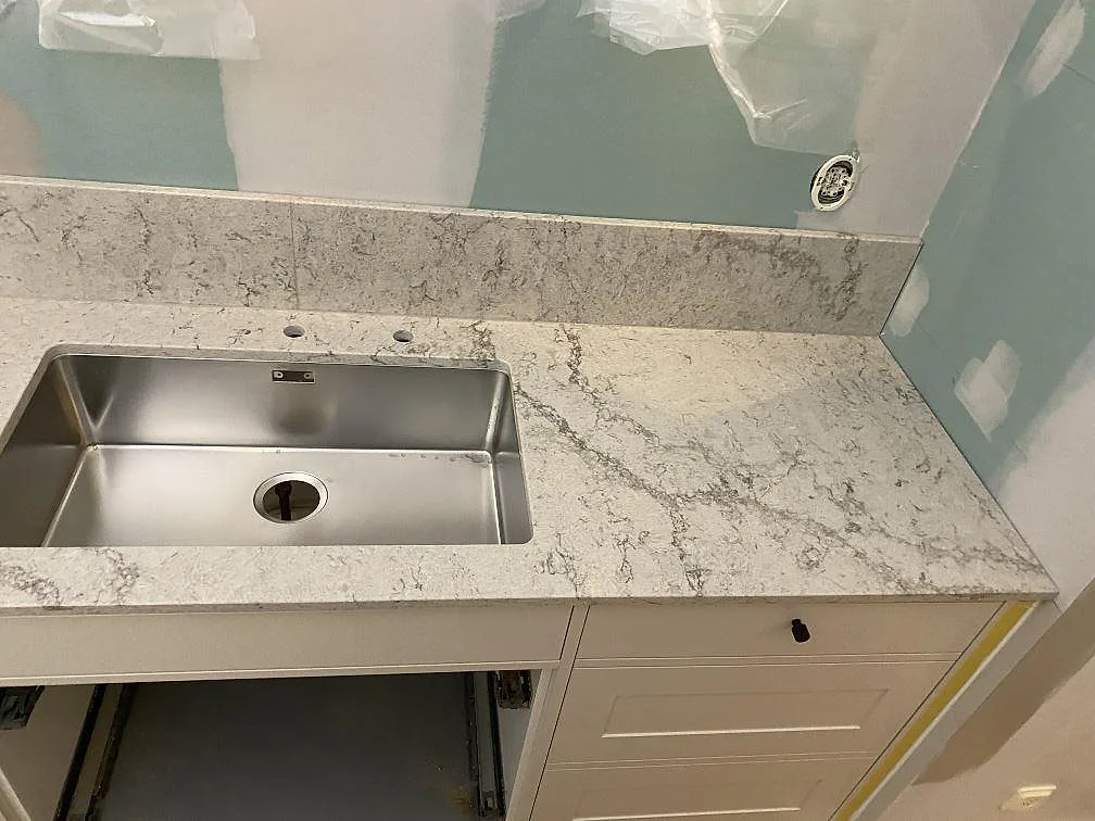 Köksbänkskiva i Caesarstone Moorland Fog med underlimmad rostfri diskho, två kranhål och stänkkant under montering i Sandared.