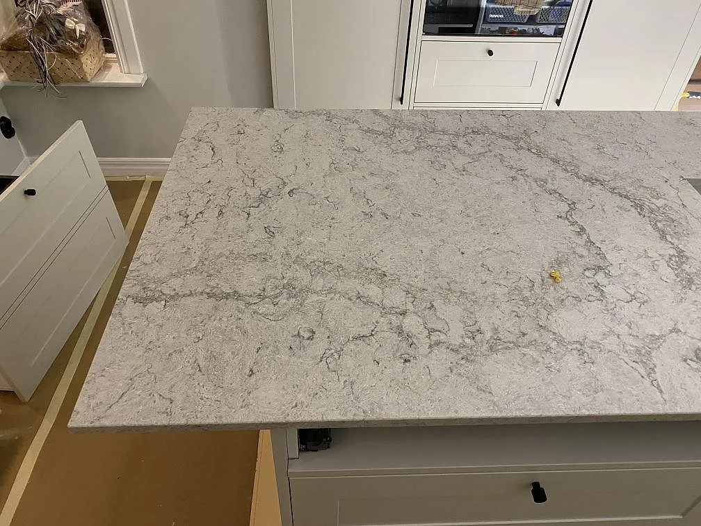 Köksbänkskiva i Caesarstone Moorland Fog, polerad ljusgrå kvartskomposit med fin grå ådring, på en stor köksö i ett kök i Sandared.