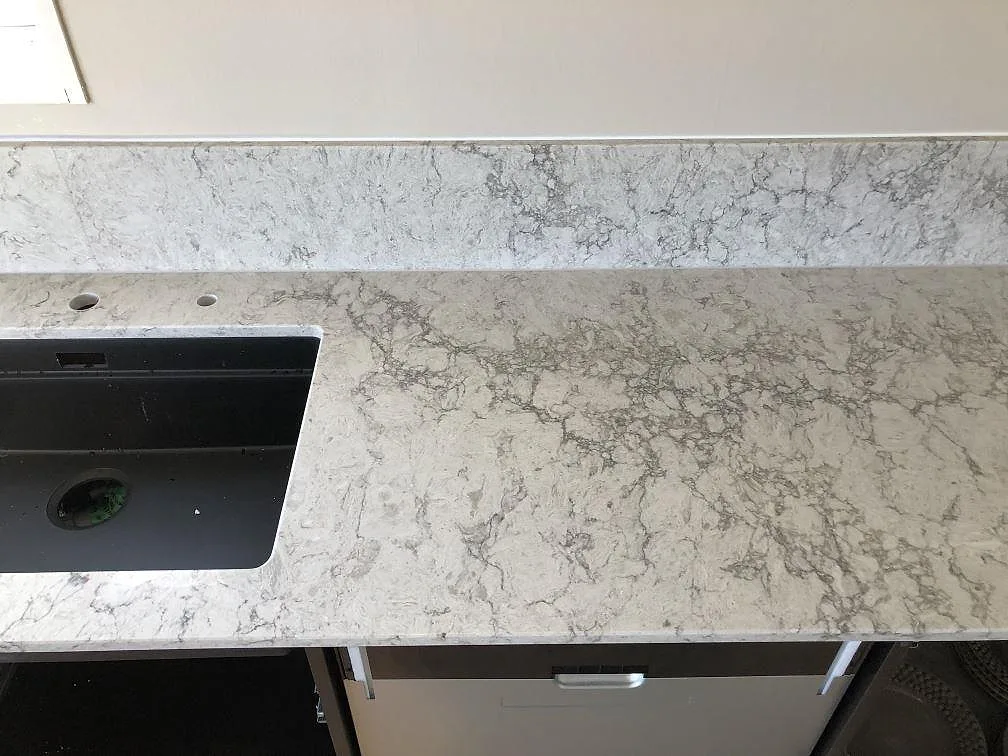 Bänkskiva i Caesarstone Moorland Fog med svart underlimmad kompositdiskho och uppvikt stänkkant i ett kök i Skegrie.