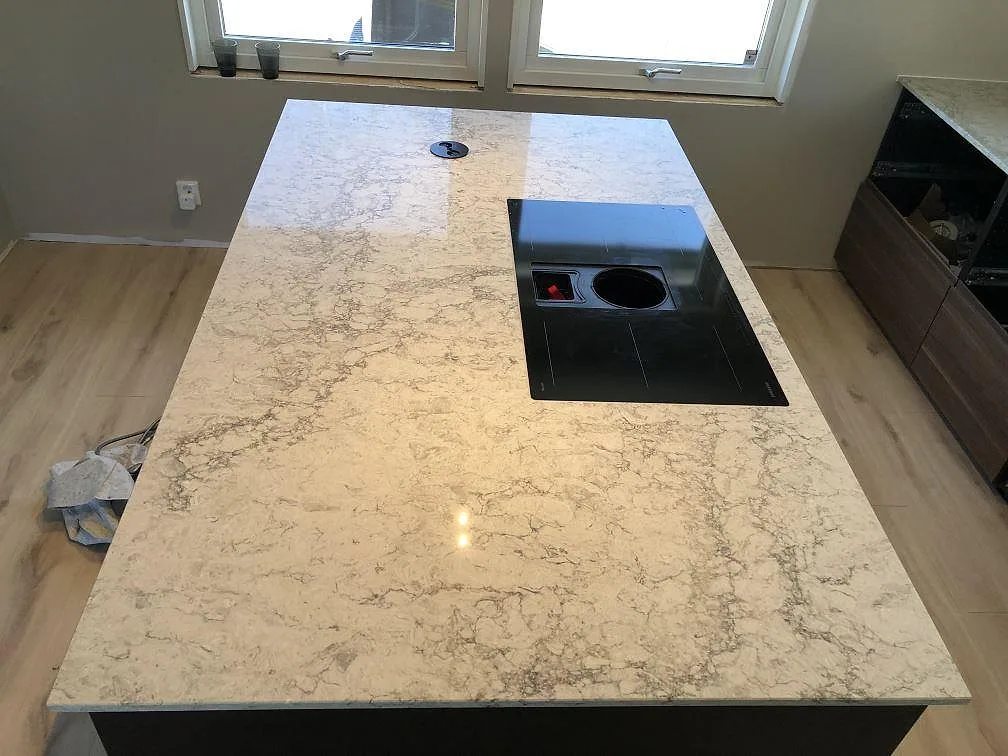 Köksö i Caesarstone Moorland Fog med nedfälld svart induktionshäll, matt yta och mjuk grå ådring i ett kök i Skegrie.