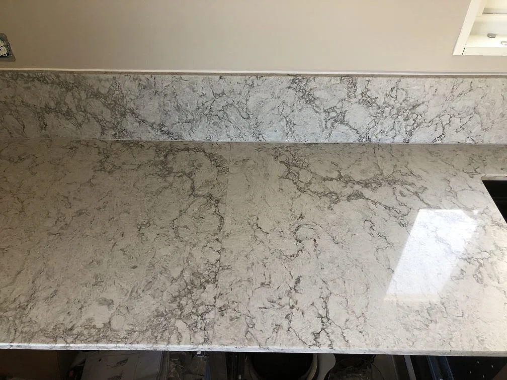 Köksbänkskiva och matchande stänkskydd i grå Caesarstone Moorland Fog med tydlig grå ådring i ett kök i Skegrie.