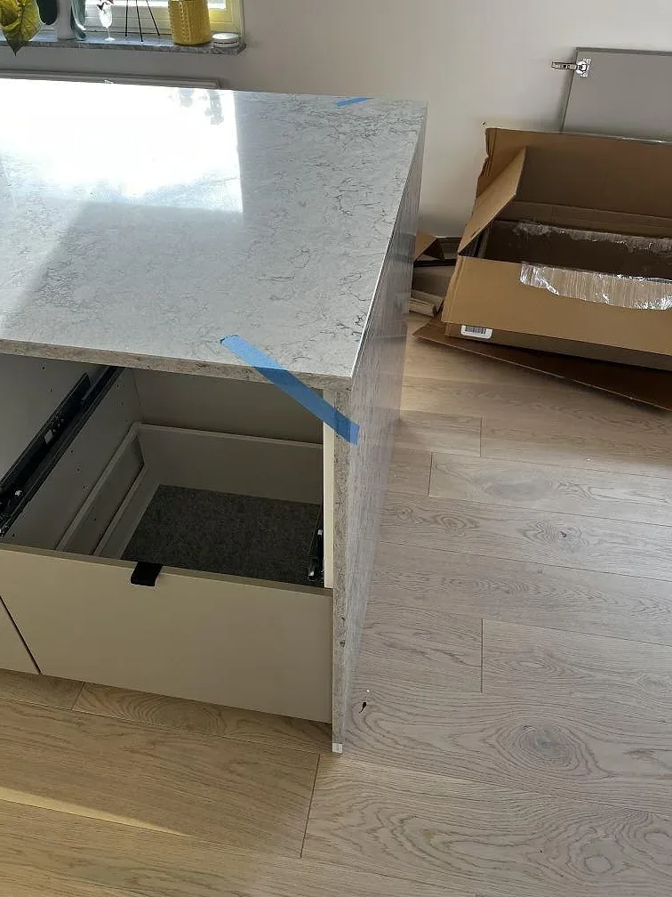 Vattenfallssida på köksö i Caesarstone Moorland Fog, polerad kvartskomposit med grå ådring under montering i Skurup.