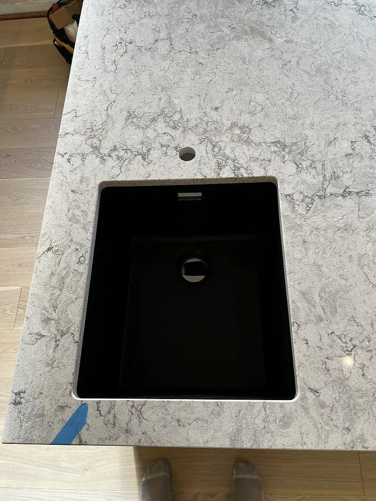 Närbild av svart underlimmad diskho och kranhål i köksö av Caesarstone Moorland Fog, polerad kvartskomposit i Skurup.