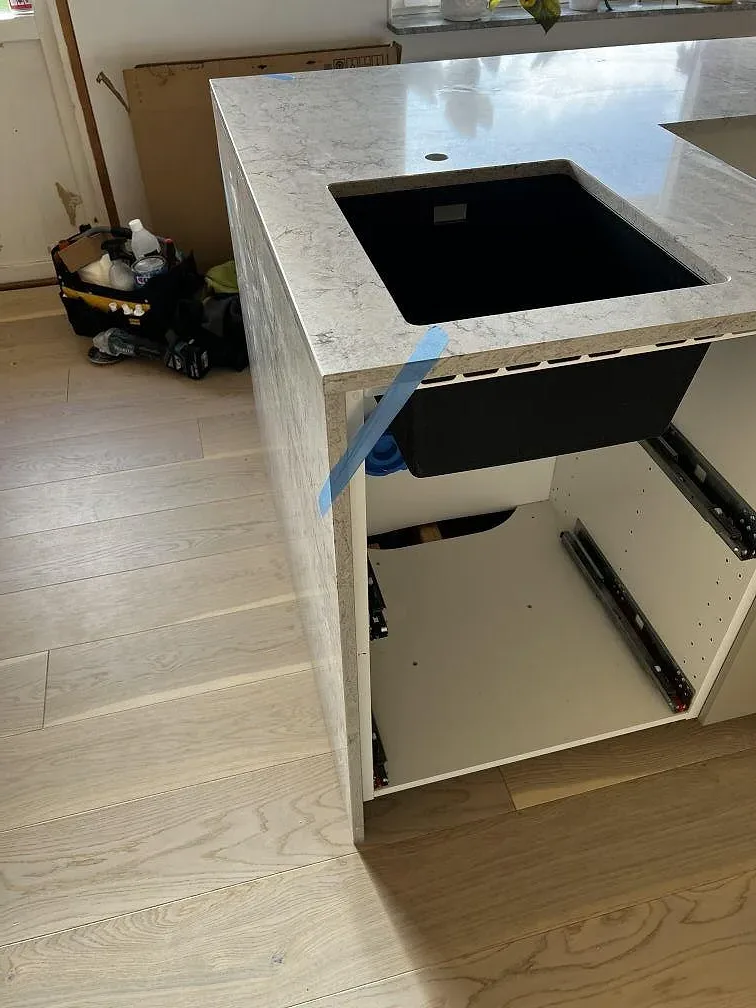 Sidovy av köksö i Caesarstone Moorland Fog med svart diskho monterad under stenen och öppna stommar i Skurup.