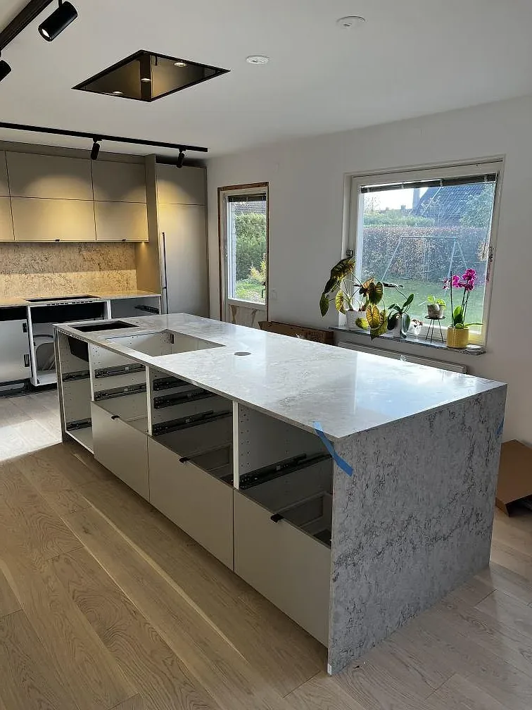 Köksö och väggbänk i Caesarstone Moorland Fog, polerad ljusgrå kvartskomposit med svart underlimmad diskho i ett kök i Skurup.