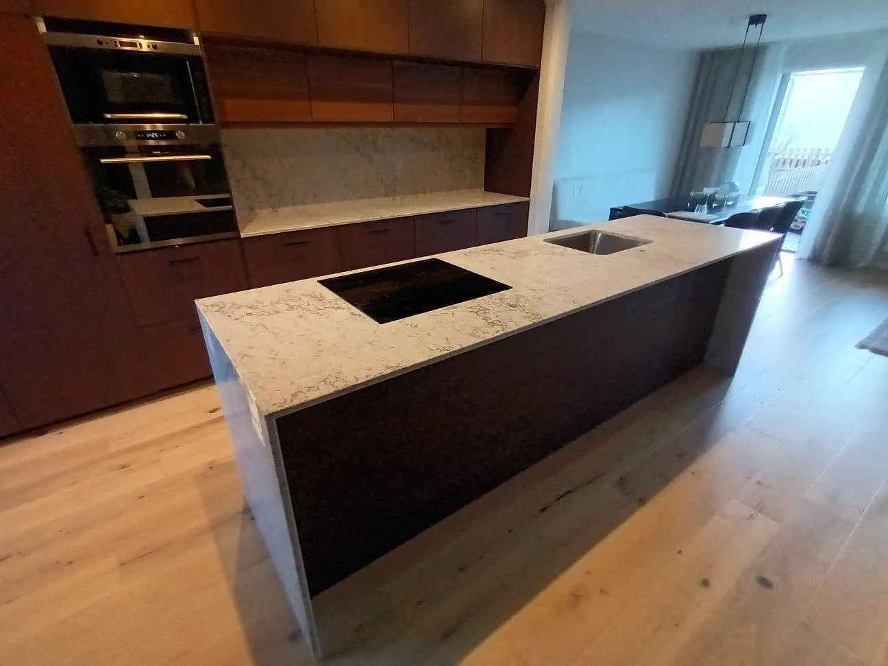 Köksö med bänkskiva i Caesarstone Moorland Fog, polerad komposit, monterad häll och rostfri diskho i ett kök i Sollentuna.