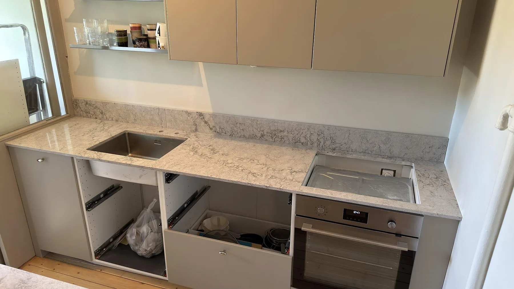 Underlimmad rostfri diskho och uppvikt stänkkant i Caesarstone Moorland Fog, polerad ljusgrå kvartskomposit, längs väggbänken i ett kök i Stockholm.
