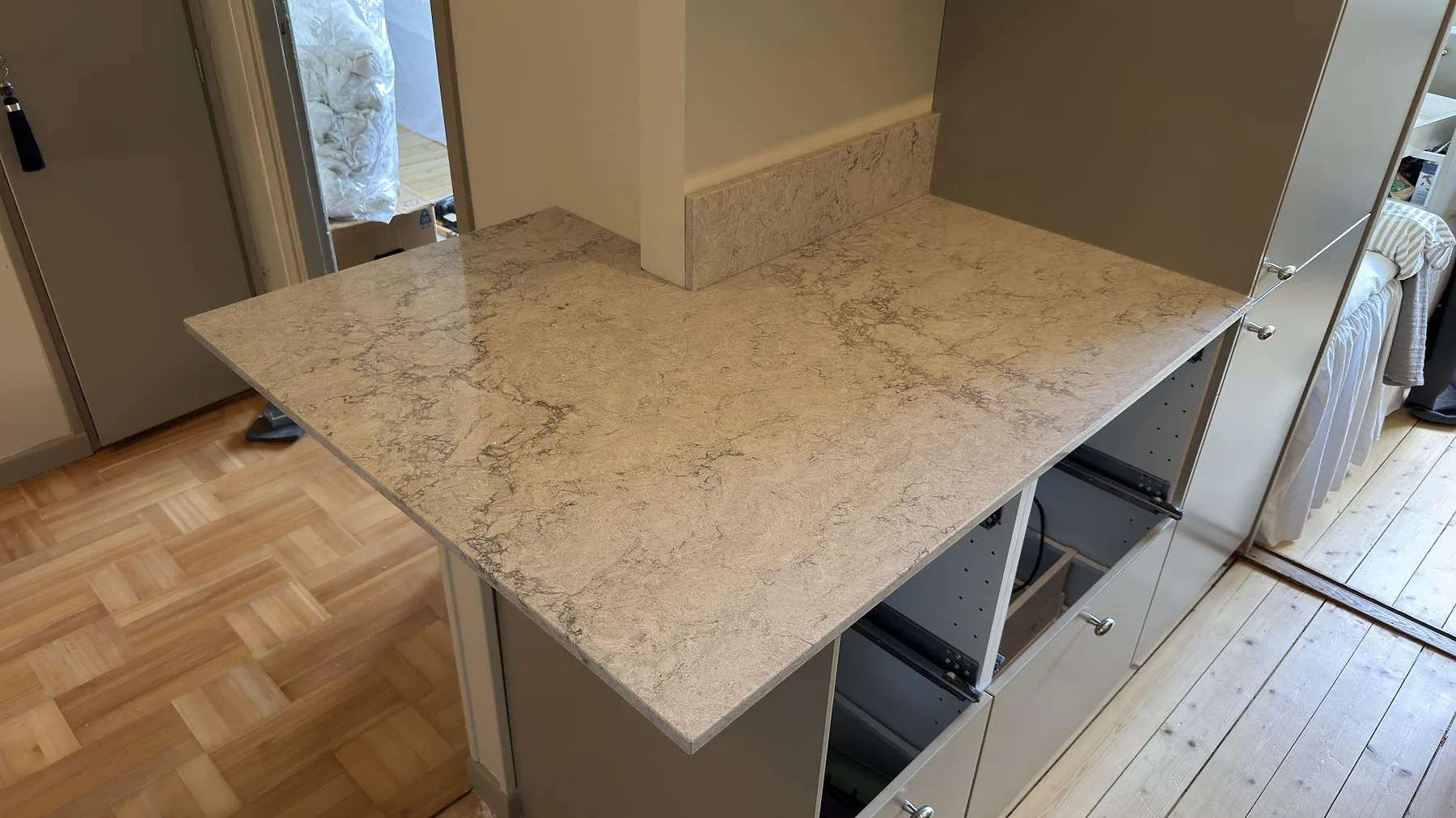 Polerad bänkskiva i Caesarstone Moorland Fog på köksön sedd från matplatsen, ljusgrå kvartskomposit i ett kök i Stockholm.