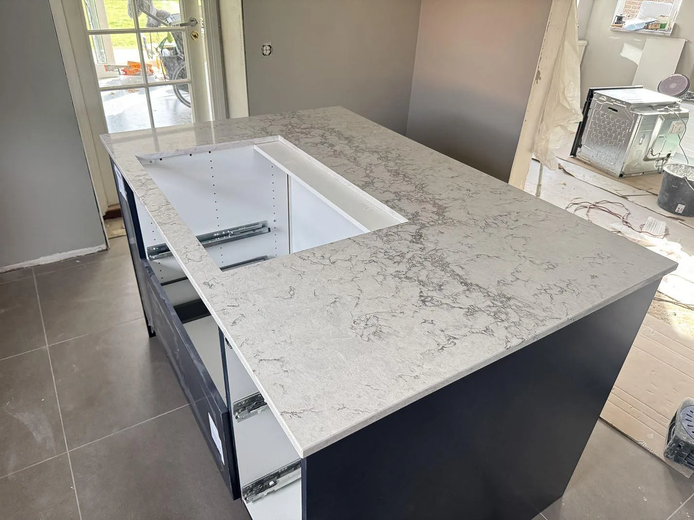 Polerad köksö i Caesarstone Moorland Fog med centralt hällurtag och öppna köksstommar under montering i Svedala.