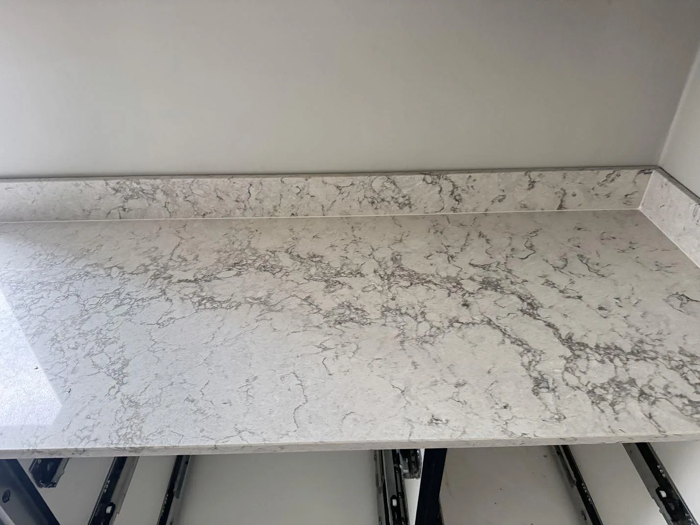 Rak bänkyta och låg stänkkant i polerad Caesarstone Moorland Fog, ljus kvartskomposit, längs en köksvägg i Svedala.