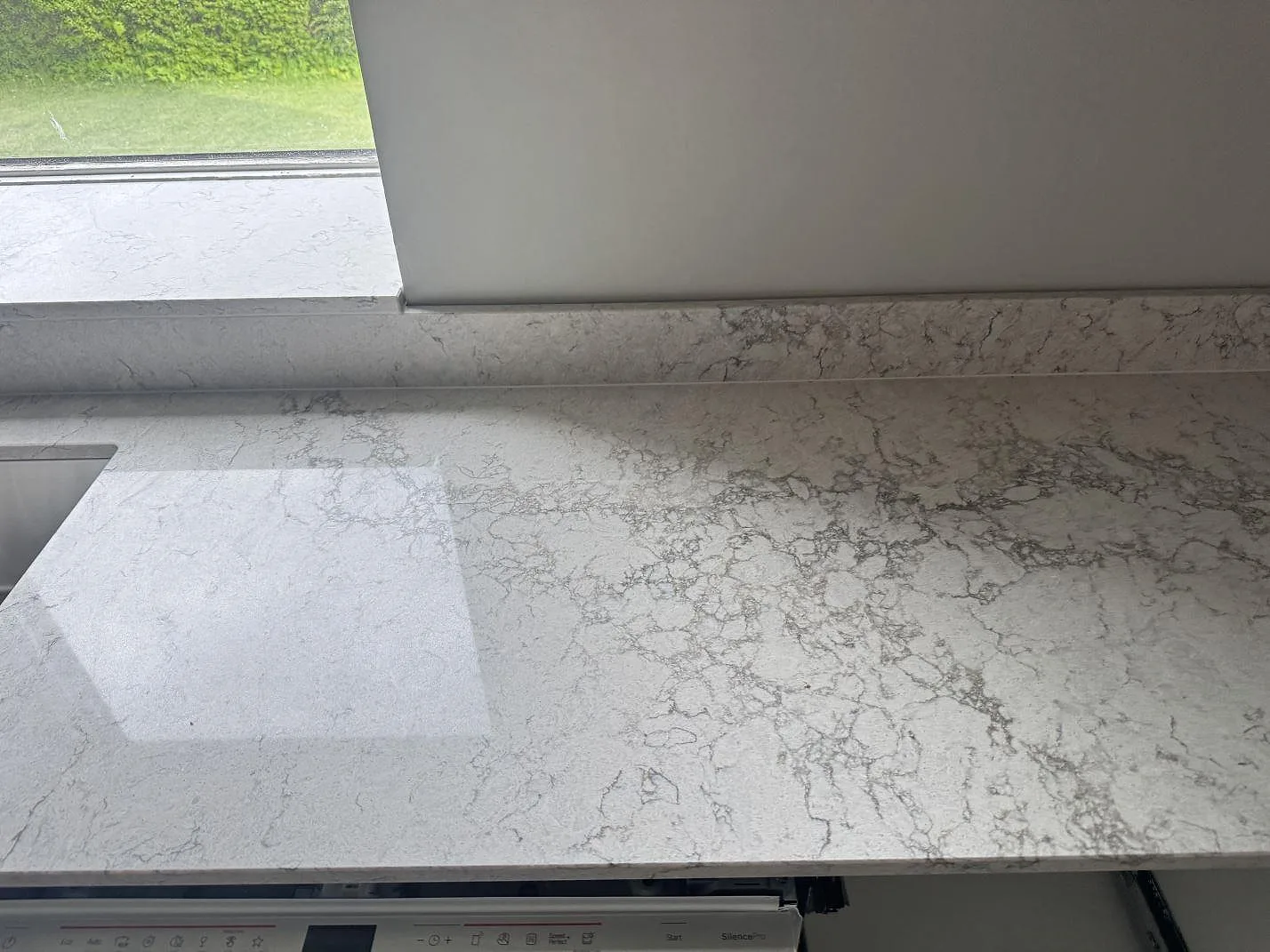 Bänkskiva vid fönster i polerad Caesarstone Moorland Fog med uppvikt stänkkant och diskho i ett kök i Svedala.