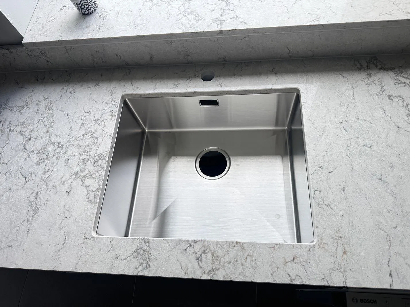 Rostfri diskho i en polerad köksbänkskiva av Caesarstone Moorland Fog, ljus kvartskomposit med grå ådring, i Svedala.