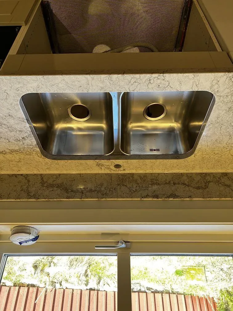 Två underlimmade rostfria diskhoar i köksbänkskiva av Caesarstone Moorland Fog framför fönstret i ett kök i Trensum.